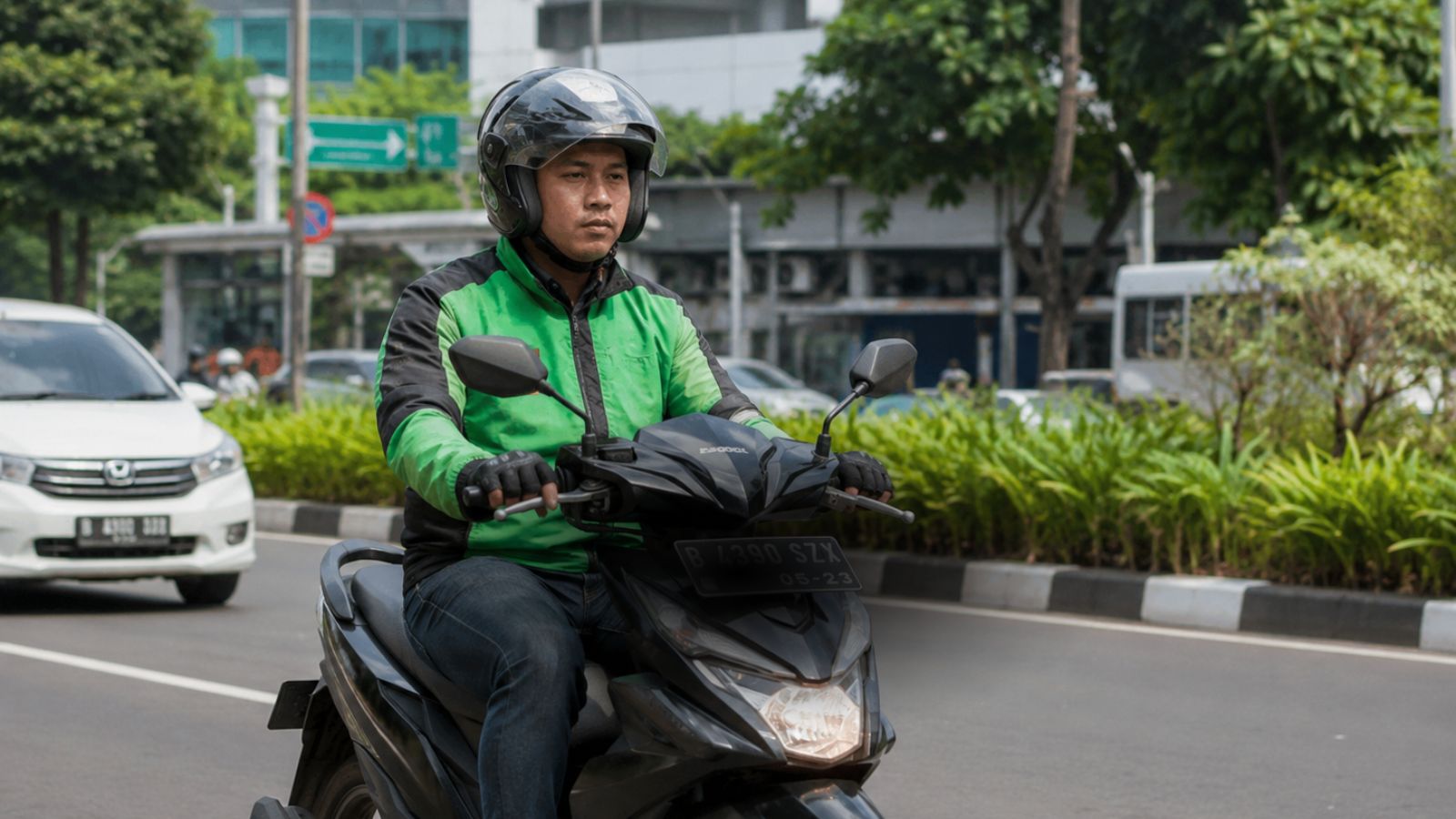 Driver ojek online memegang pinggang sambil berhenti di tepi jalan setelah berkendara lama.